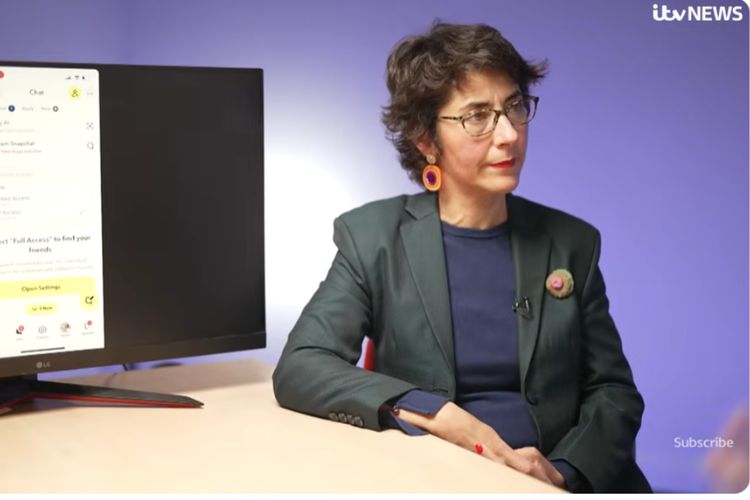 A woman wearing a dark suit, glasses and with dark hair (elvira perez vallejos) is sitting at a desk beside a computer monitor