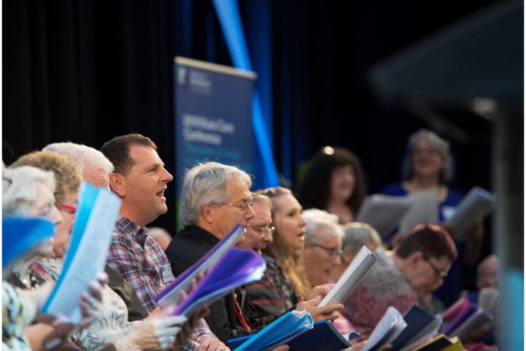 A group of people are singing together, holding song-sheets,