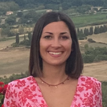 Person in pink dress leaning against a wall with fields in the background