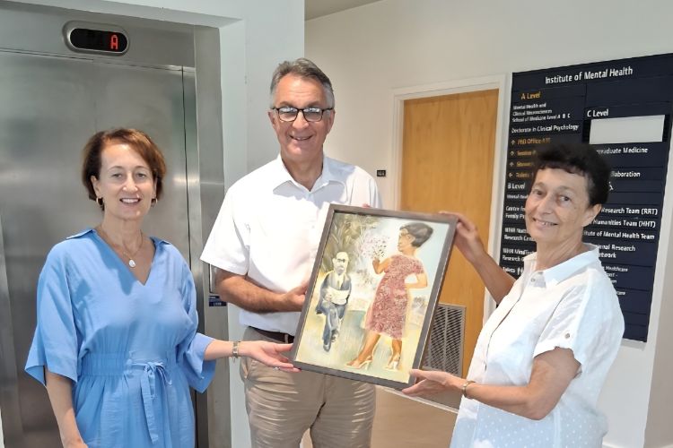 3 people smiling at the camera. The person in the centre (Martin Orrell) is being presented with a painting my the two people either side