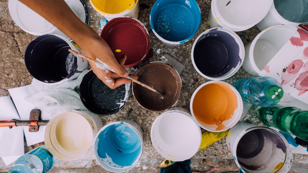 lots of open pots of paint with a person dipping their brush into one of the pots